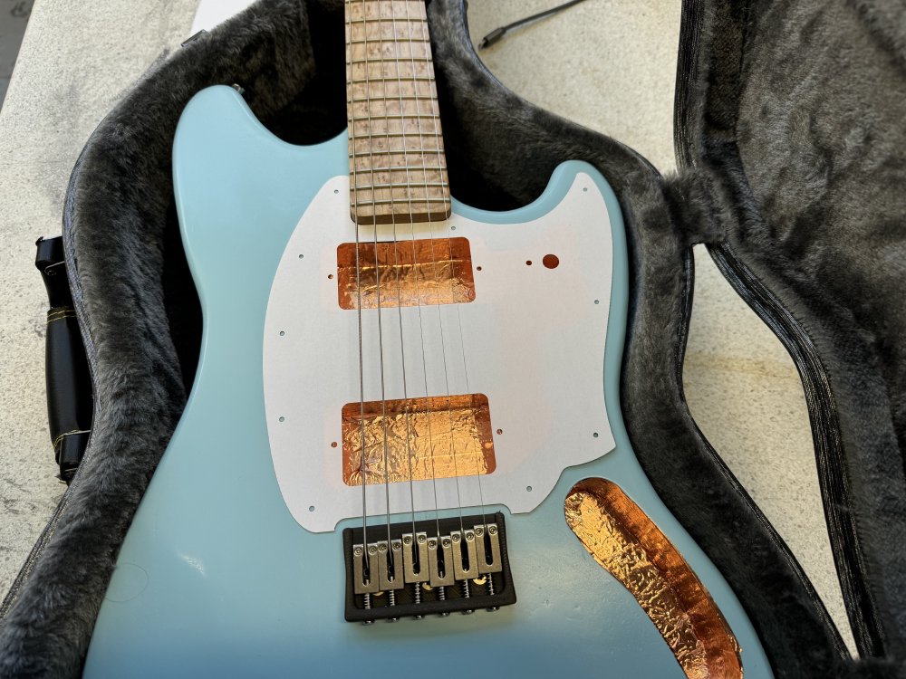 A photo of a guitar with a paper pick-guard installed, mocking out where the pick-guard will eventually sit.