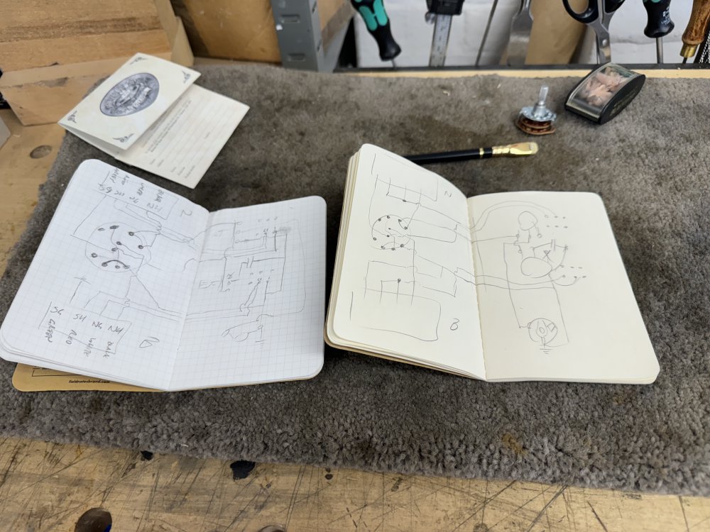 A photo of two small notebooks sat side by side on a workbench. Each has a similar circuit diagram that spans two pages, but they are not identical, with one lacking writing on it and having different lines connecting the parts.