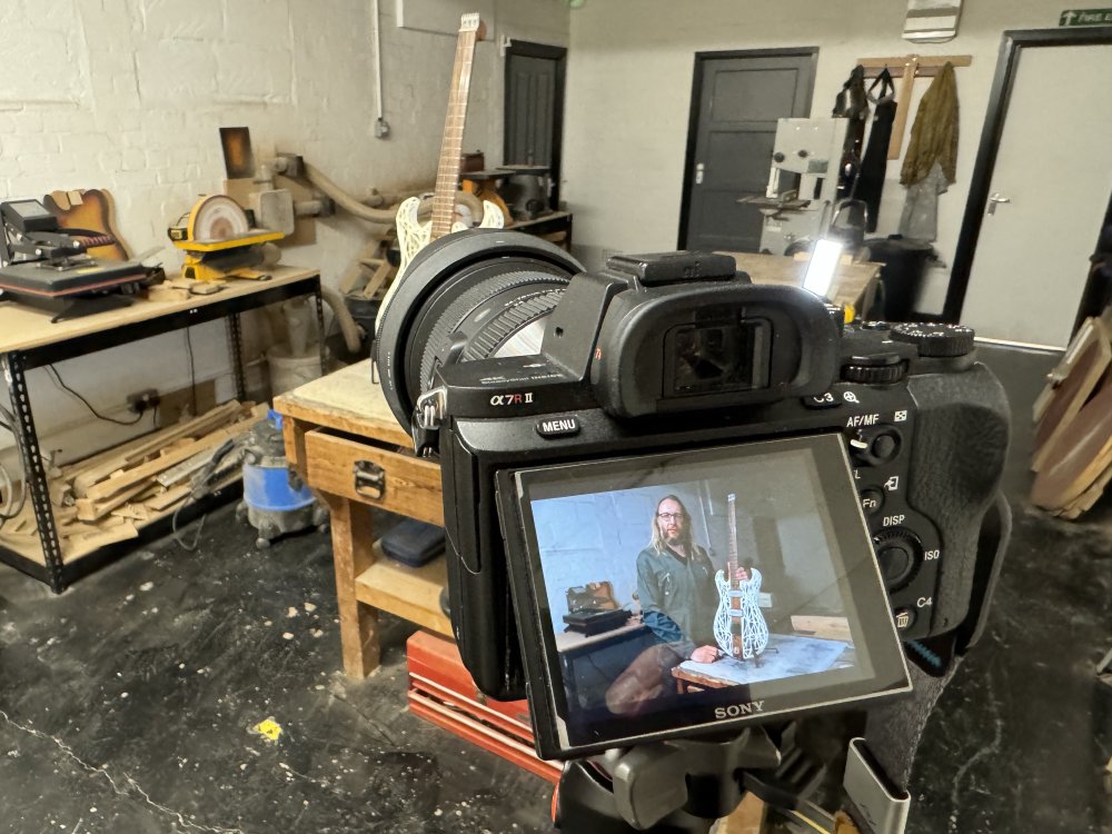 A photo again of a camera on a tripod in the workshop, pointing at a guitar on the workbench behind. On the screen of the back of the camera you can see the guitar, but also me stood next to it, despite the fact I'm no longer in the scene behind the camera.