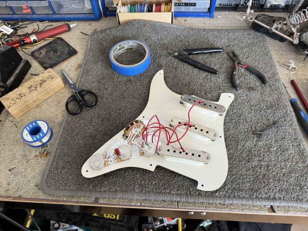 A photo of the backside of a guitar pick-guard, showing the pickups, the selector switch and volume and tone pots, with a lot of wires running between them.