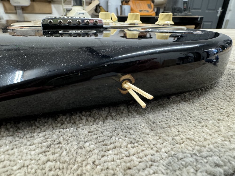 A photo of the bottom end an electric guitar body, and where the strap-button should be is a hole with three tooth-picks sticking out of it.