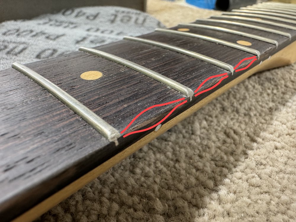 A annotated version of the previous photo, where red lines have been crudely drawn on to try indicate the way the fretboard edge is rounded over and then not between the frets.