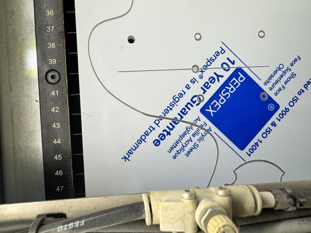 A photo of the sheet of acrylic on the laser-cutter bed, show where the outline of a guitar body has been cut into the material. In the line you can see a point where the line goes from thin to thick, which is the end/start of the cut.