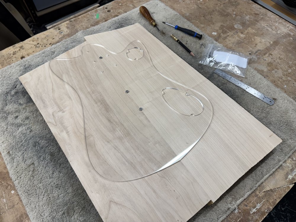 A photo of the laser-cut body template screwed on to the body blank. Again you can see the centre line of the template has been aligned with the join line on the body blank. To the side sits a pencil, a ruler, and a bradawl.