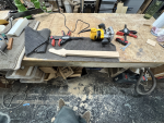 A wide-angled photo showing the work in progress neck that has been trimmed, now unclamped, and on the floor is a large amount of wood dust.