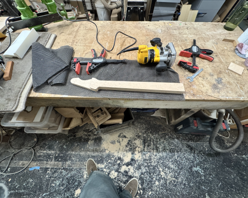 A wide-angled photo showing the work in progress neck that has been trimmed, now unclamped, and on the floor is a large amount of wood dust.