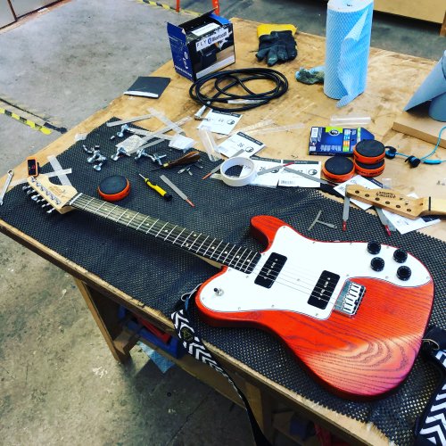 An orange telecaster-style guitar sits on the workbench, with tools and string wrappers and other bits strewn around it.