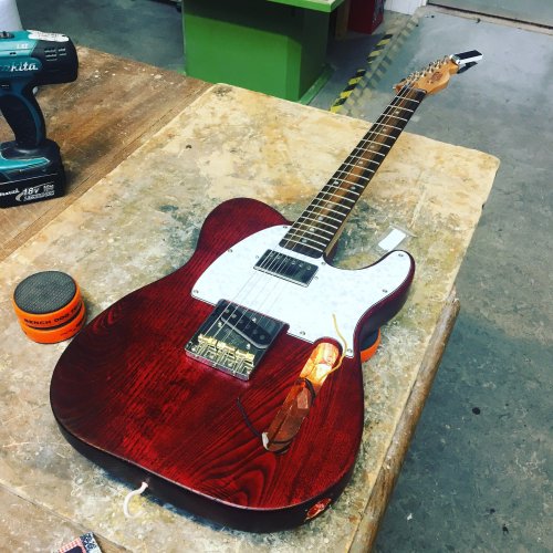 A crimson t-style guitar sites on the workbench, all complete except the electronics are still being wired in.