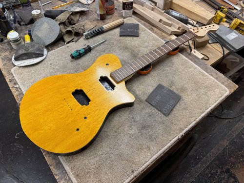 An in-progress guitar shot, showing a body with birds-eye maple cap and various bits of hardware like bridge and pickup rings laid on the body, and a maple neck with rose-wood fretboard sat in position.